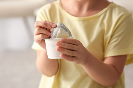 Cute little girl opening yogurt pack at home, closeupの写真素材