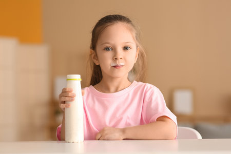 Cute little girl sitting by table with bottle of yogurt at homeの写真素材