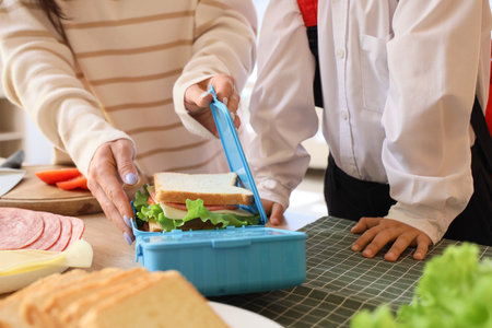 Mother with her little son packing sandwich into lunchbox in kitchen, closeupの写真素材