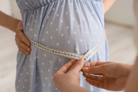 Young pregnant woman with doula measuring belly at home, closeupの写真素材