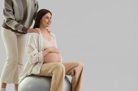 Young pregnant woman with doula sitting on fitball against light backgroundの写真素材