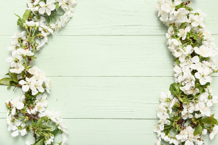 Frame made of beautiful blossoming branches on green wooden background