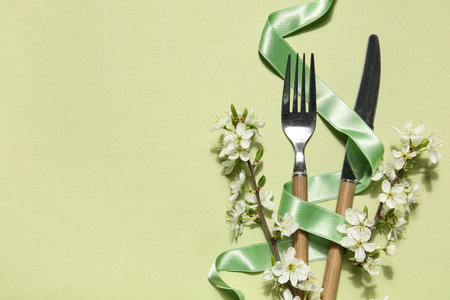Silver cutlery with ribbon and blossoming branches on green backgroundの写真素材