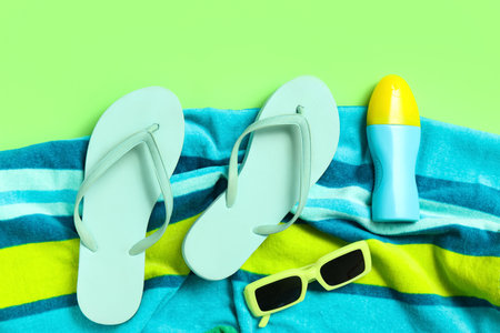 Flip flops with towel, bottle of sunscreen and sunglasses on green backgroundの写真素材