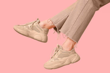 Legs of young woman in stylish beige sneakers on pink backgroundの写真素材
