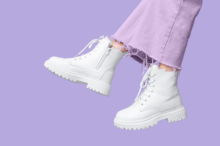 Legs of young woman in stylish white leather boots on lilac backgroundの写真素材