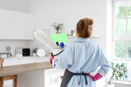 Mature woman with cleaning supplies in kitchen, back viewの写真素材