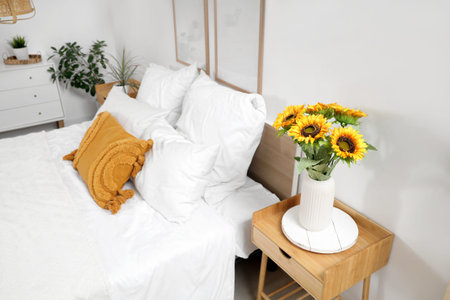 Interior of light bedroom with cozy bed and beautiful sunflowers on bedside tableの写真素材