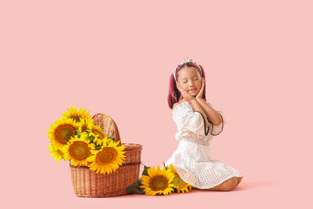 Cute little Asian girl with beautiful sunflowers in wicker basket sitting on pink backgroundの写真素材