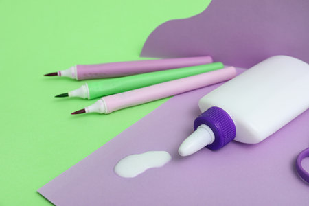 Bottle with spilled glue, felt-tip pens and sheet of paper on green backgroundの写真素材