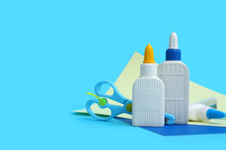 Bottles of glue, scissors and sheet of paper on blue backgroundの写真素材