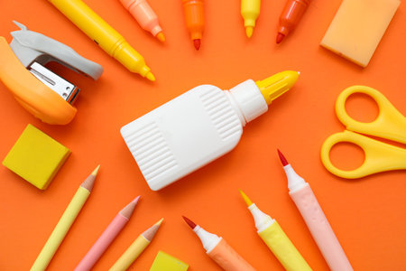 Bottle of glue, scissors and felt-tip pens on orange background. Top viewの写真素材