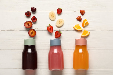 Sports bottles of fresh juice with different fruits on white wooden backgroundの写真素材