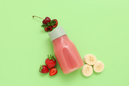 Sports bottle of fresh strawberry juice with cherries and banana on green backgroundの写真素材