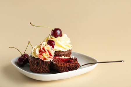 Plate with sweet cherry cupcakes and berries on beige background