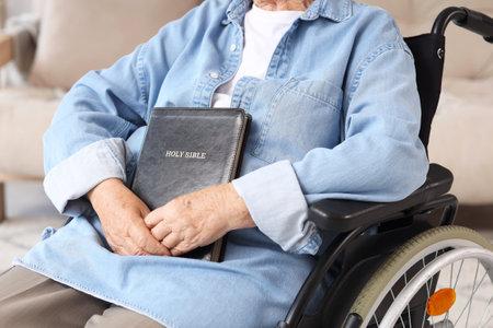 Senior woman in wheelchair with Bible at home, closeupの写真素材
