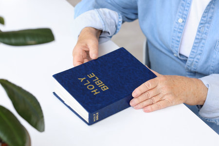 Senior woman with Bible sitting at table in living room, closeup