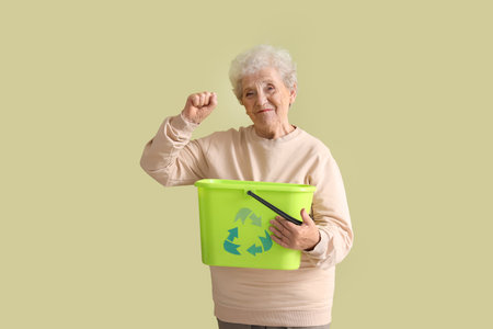 Senior woman with garbage bin on green background. Waste sorting conceptの写真素材