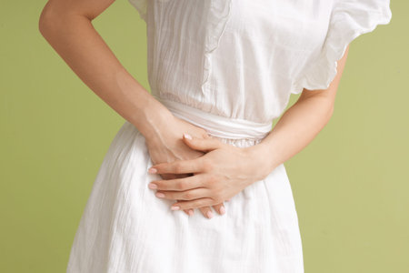 Young woman suffering from severe abdominal pain on green background, closeup