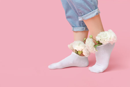 Legs of young woman in white socks with eustoma flowers on pink background