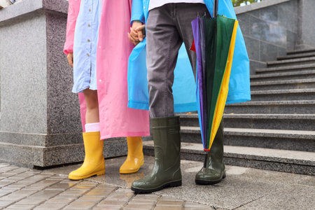 Couple wearing raincoats and gumboots on rainy day outdoors