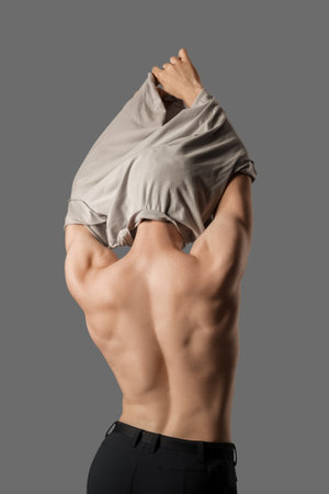 Muscular young man taking off his shirt on gray background, back viewの写真素材