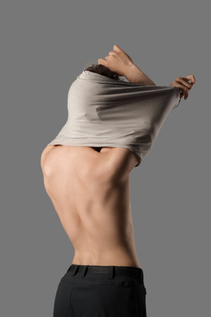 Muscular young man taking off his shirt on gray background, back viewの写真素材