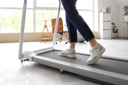 Young businesswoman training on treadmill in office, closeup