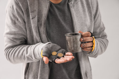 Young homeless man with cup and coins on light background, closeupの写真素材
