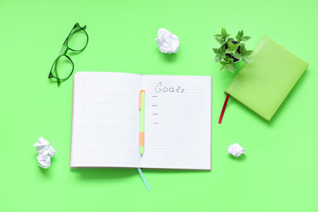Notebook with list of goals, crumpled paper and pen on green background