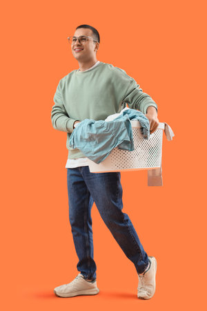 Young man holding basket with laundry on orange backgroundの写真素材