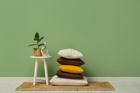 Stack of cushions on carpet and plant with human figure on coffee table near green wall in roomの写真素材