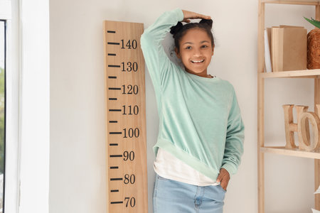 Little African-American girl measuring height near stadiometer at homeの写真素材
