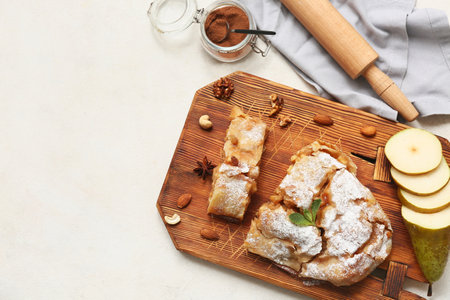 Wooden board with pieces of tasty pear strudel, cut fresh fruit and rolling pin on beige backgroundの写真素材