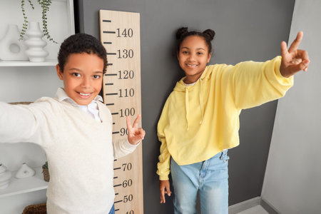 Little African-American children taking selfie near stadiometer at home