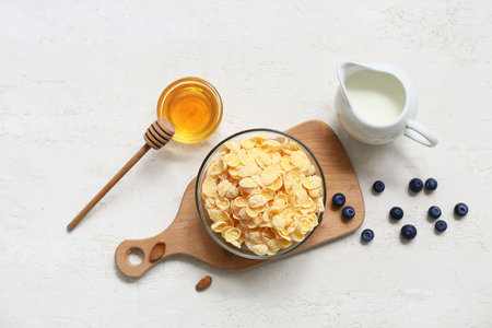 Wooden cutting board, honey, bowl with cornflakes and berries on light backgroundの写真素材
