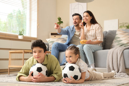 Happy family with popcorn and soccer balls watching football game at homeの写真素材