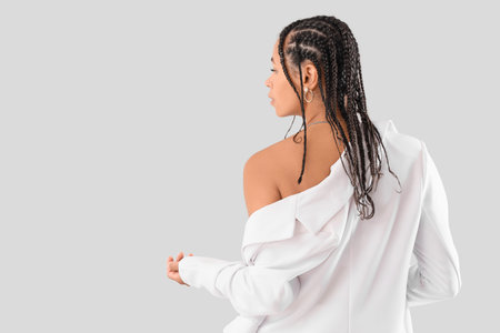 Stylish African-American woman with dreadlocks on light background, back view