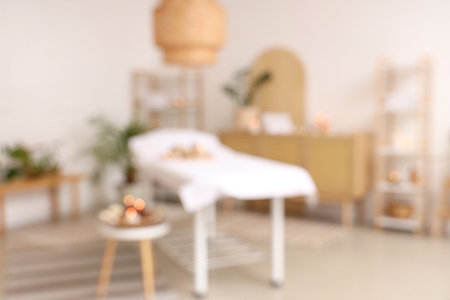 Blurred view of light spa salon with massage couch, burning candles and shelf unitsの写真素材