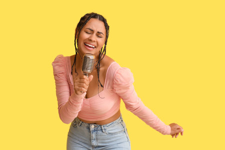 Young African-American woman with microphone singing on yellow backgroundの写真素材