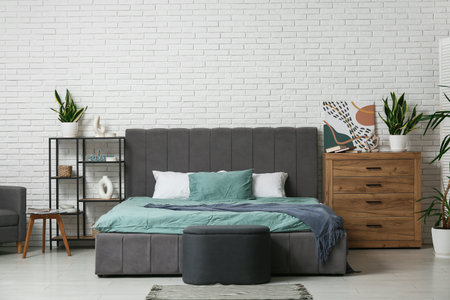 Interior of stylish bedroom with big bed, shelf unit and drawers