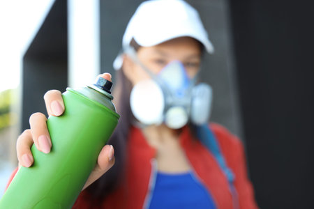 Young woman in respirator with spray paint can on street, closeup
