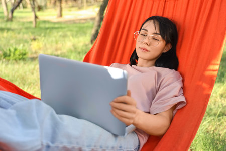 Young woman using laptop in hammock outdoorsの写真素材