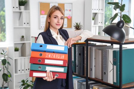 Young businesswoman with document folders near shelf unit in officeの写真素材