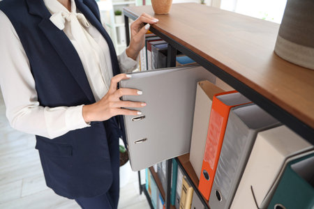 Young businesswoman taking document folder from shelf in office, closeup