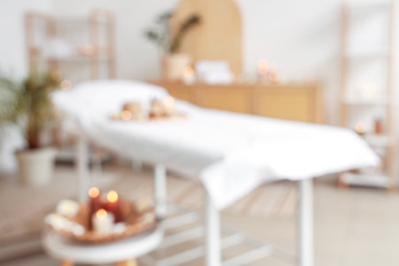 Blurred view of light spa salon with massage couch, burning candles and shelf unitsの写真素材
