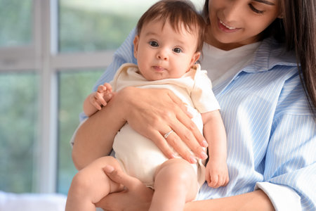 Mother holding her little baby near window at home, closeupの写真素材