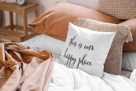 Big comfortable bed with crumpled linen and pillow with text THIS IS OUR HAPPY PLACE in room....