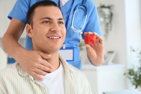 Female endocrinologist with thyroid gland model and male patient in clinic, closeup