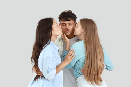 Young man with two women kissing on light background. Polyamory conceptの写真素材